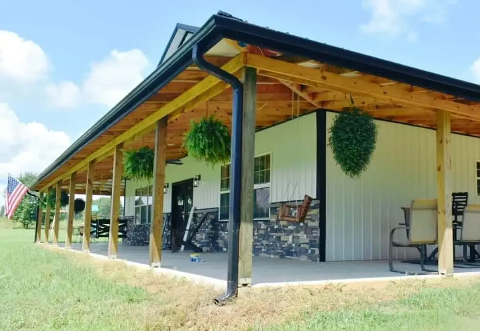 Covered timber porch with hanging ferns on a barndominium